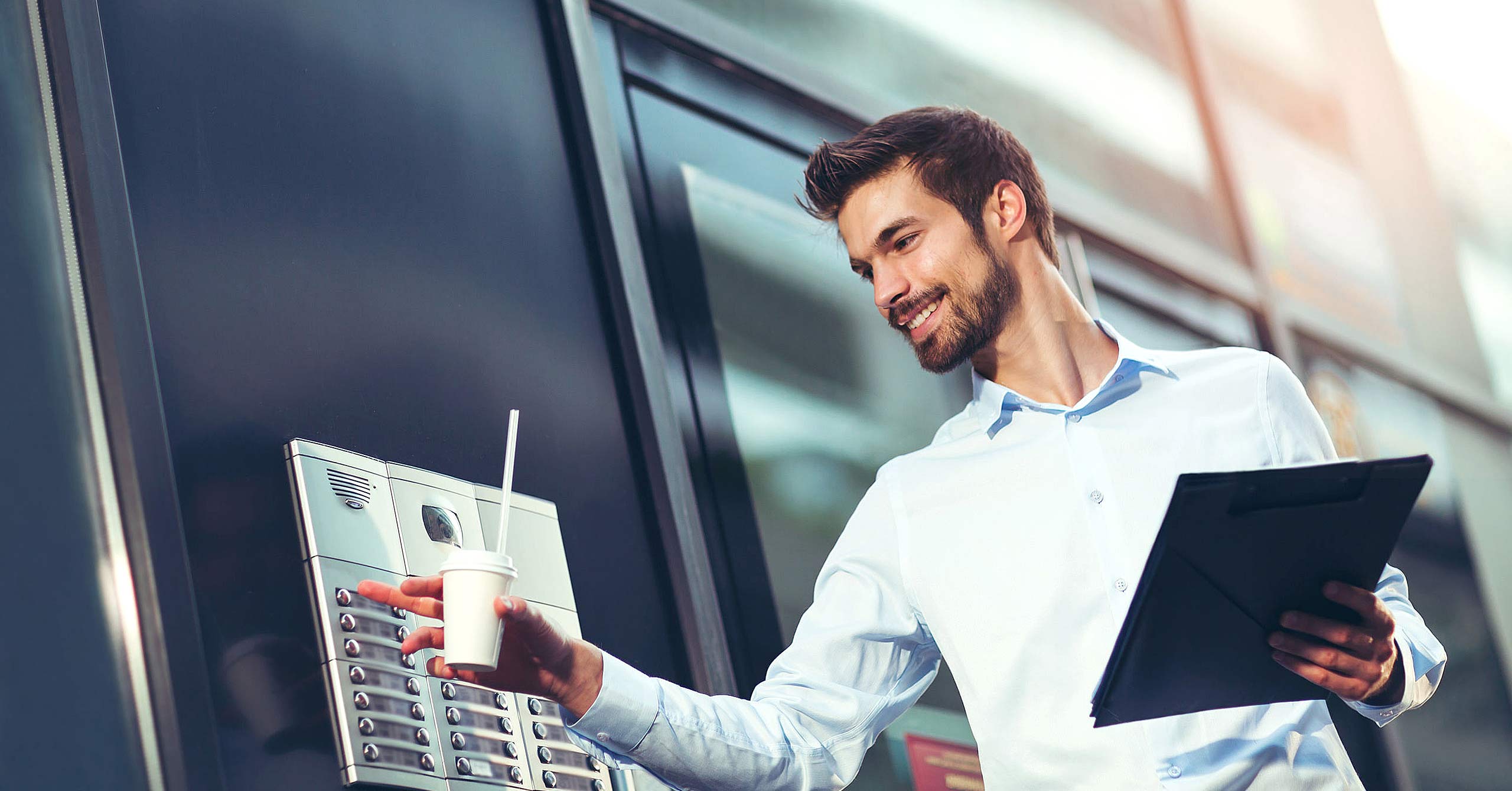 Portrait of a young happy businessman who is ringing the bell at a intercom